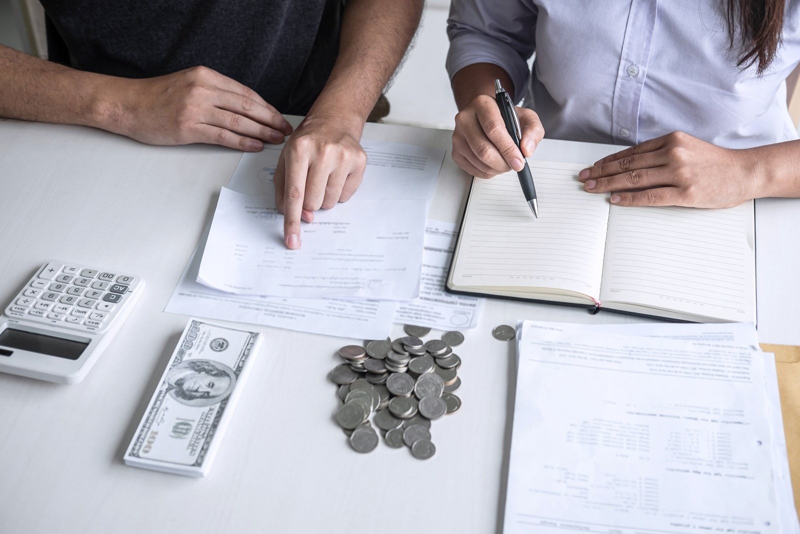 Two people reviewing bills and making notes beside a calculator