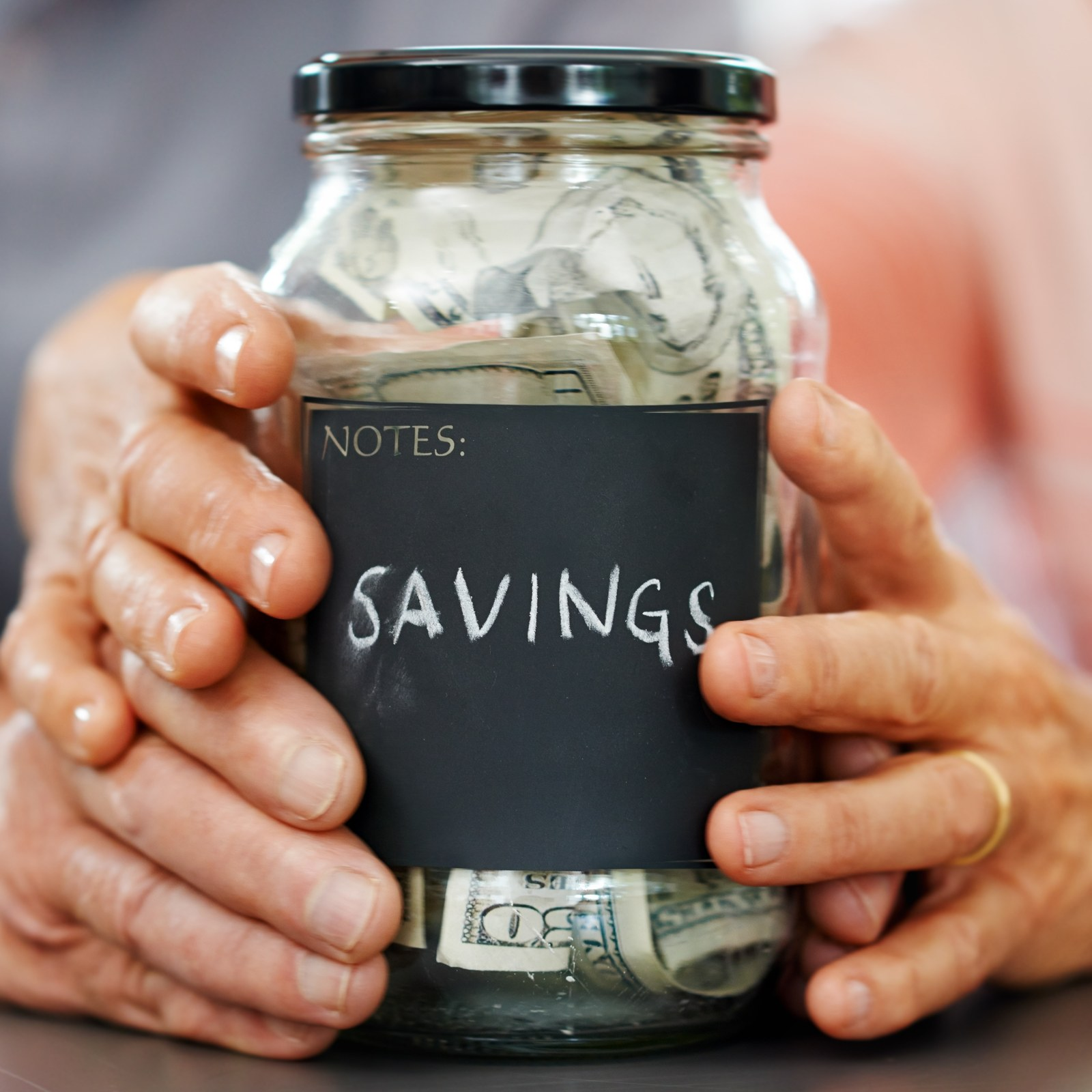 Hands holding a glass savings jar filled with money