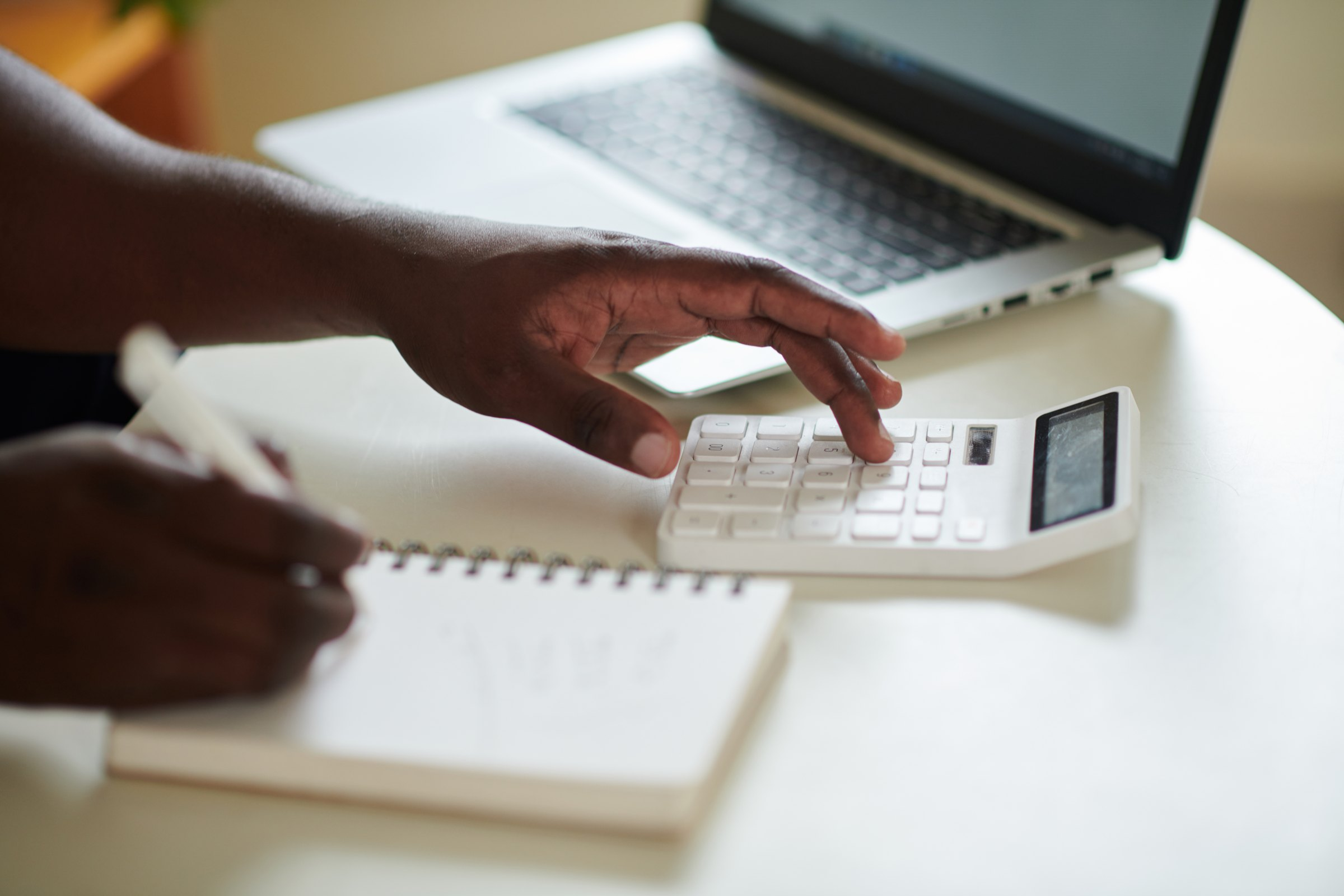 Hands using a calculator beside a notebook and laptop