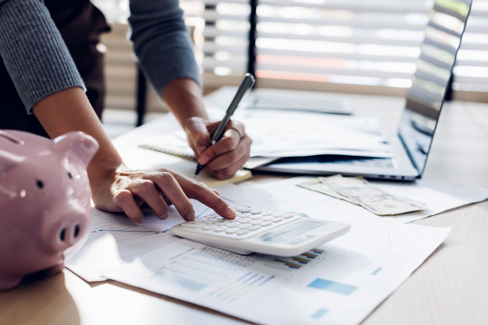A person using a calculator and making notes beside financial paperwork