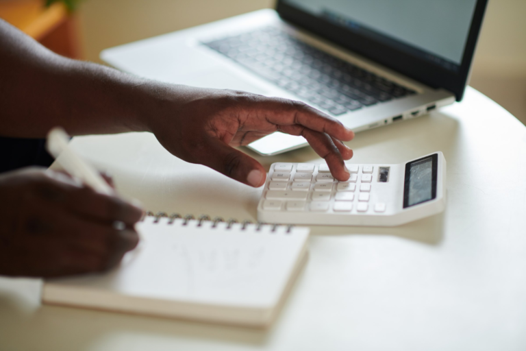 Hands using a calculator beside a notebook and laptop